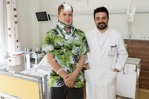 Ein Patient mit Kopfverband und Halskrause steht neben einem Arzt